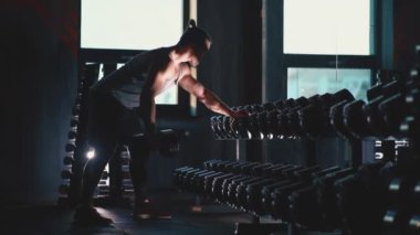 Mükemmel gövdeli atletik adam spor salonunda dambıllarla egzersiz yapıyor.