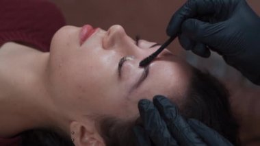 Güzellik salonunda kadın kaşlarını fırçayla tarayan eldiven giymiş bir güzellik uzmanı.