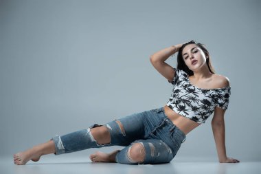 Stüdyoda gri arka planda kot pantolonla poz veren çekici bir kadın.