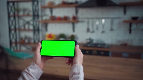 Closeup dari tangan perempuan menggunakan smartphone dengan layar hijau mockup di dapur rumah — Stok Video