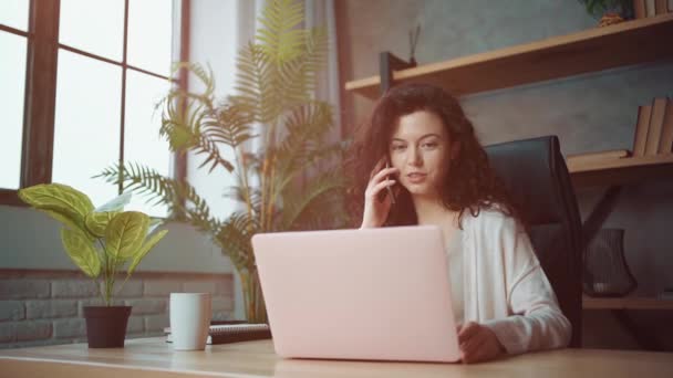 Fröhliche Managerin, die mit Laptop arbeitet und zu Hause mit dem Handy telefoniert — Stockvideo