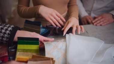 Kadın müşterilerin elleri tekstil galerisinde perde için kumaş seçiyor.