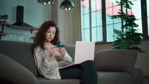 Jovem fêmea fazer compra on-line com cartão de crédito e laptop no sofá em casa — Vídeo de Stock