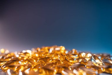 Mavi arka planda bir avuç altın balık yağı kapsülü Omega 3 vitamini