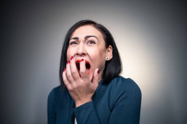 Stüdyoda, gri arka planda korkmuş esmer bir kadın var.