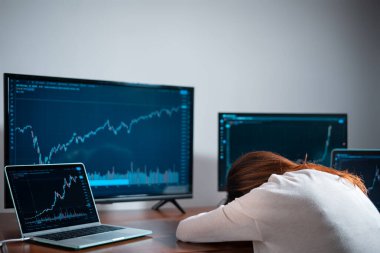 Yeni başlayan yorgun kadın tüccar iş yerinde hisse senedi grafiğiyle monitörün yanında uyuyor.