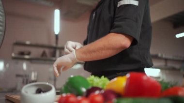 Erkek aşçı sebze salatası hazırlarken koruyucu eldiven giyer.