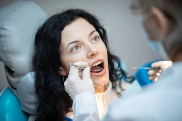 Bela morena encaracolado feminino dentista tratar paciente na clínica moderna — Fotografia de Stock