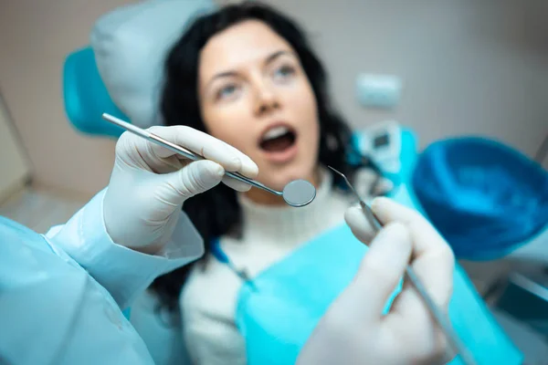 Bela morena encaracolado feminino dentista tratar paciente na clínica moderna — Fotografia de Stock