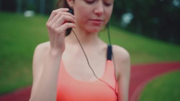 运动后，年轻的女跑步者带着耳机在室外听音乐 — 图库视频影像