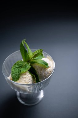 Lezzetli vanilyalı dondurma, siyah arka planda cam kasede taze nane şekeri.