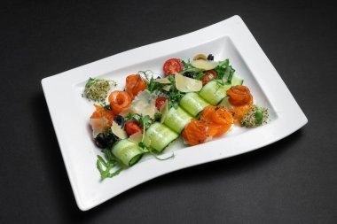 Hafif tuzlu somon ve siyah arka planda sebzeli salata yakın plan.