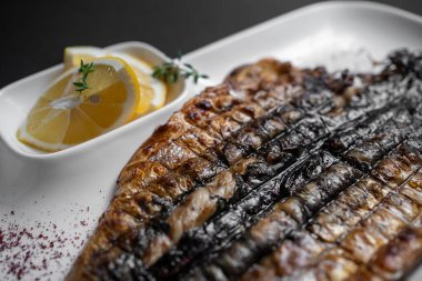 Siyah arka planda beyaz tabakta limonlu ızgara uskumru balığına yakın plan.