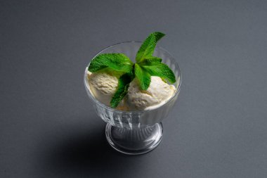 Lezzetli vanilyalı dondurma, siyah arka planda cam kasede taze nane şekeri.