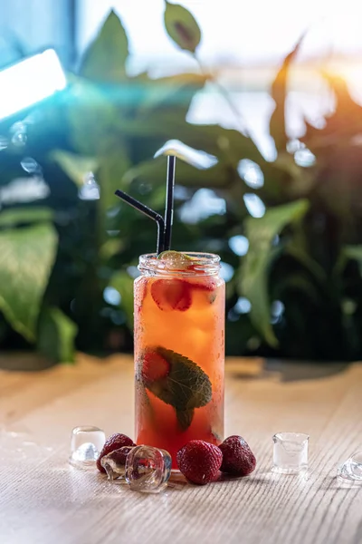 Aardbeienlimonade drinken met munt in glazen fles en ijs in de buurt van groene plant — Stockfoto