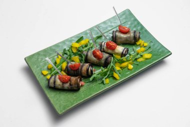 Beyaz arka planda yeşil tabakta krem peynirli patlıcan rulolarını kapat.