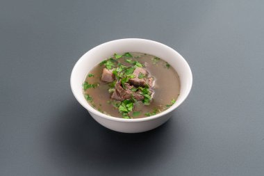 closeup of bone broth with beef meat and parsley in bowl on grey background