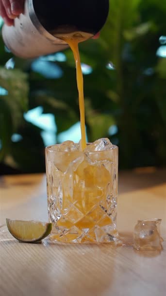 Ручной налив желтого сока в стакан со льдом или приготовление холодного коктейля — стоковое видео