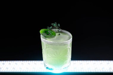 Taze yeşil kivi siyah arka planda şarap kadehinde alkollü kokteyl içkisini tekmeliyor.