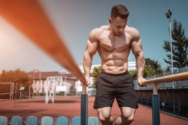 Çekici kaslı sporcu ya da vücut geliştiren adam kenara çekilip dışarıda egzersiz yapıyor.