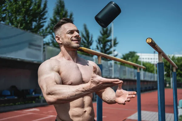 Muskulöser Sportler wirft schwarzen Behälter mit Protein-Molkenpulver in die Luft — Stockfoto