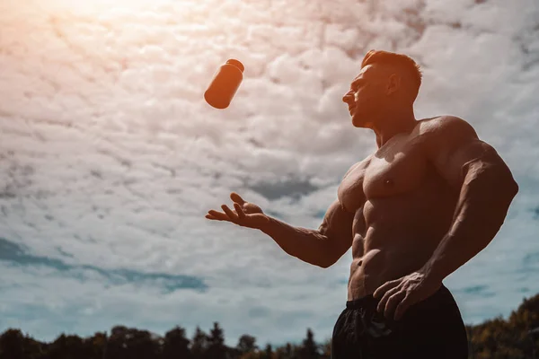 Muskulöser Sportler wirft schwarzen Behälter mit Protein-Molkenpulver in die Luft — Stockfoto