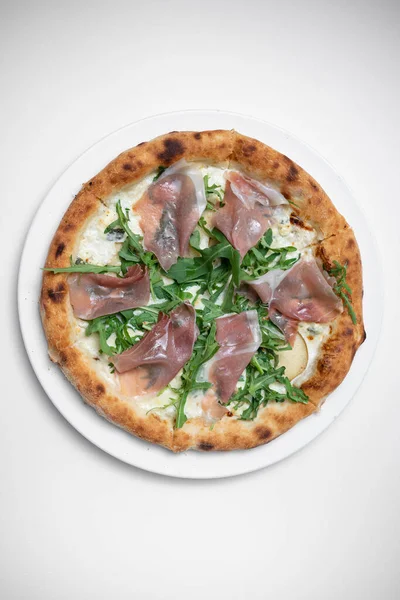 Beyaz arka planda prosciutto, roka ve peynirli lezzetli pizzanın üst görüntüsü.