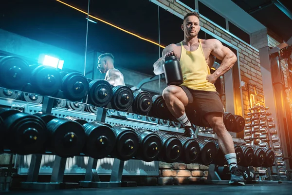 Vücut geliştiren kaslı erkek, spor salonunda siyah kabın içinde protein tozuyla.