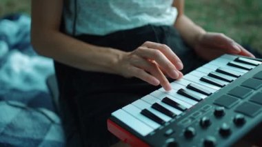 Midi klavye sentezleyicisi çalan ve açık havada müzik besteleyen bir kız eli.