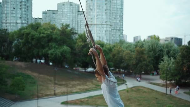 Garoto ativo balançar no bungee caseiro na árvore ou se divertir no parque da cidade ao ar livre — Vídeo de Stock