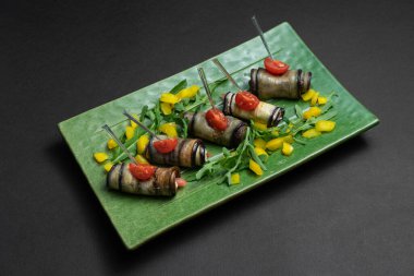 Patlıcan rulolarını, krem peynirle, yeşil tabakta, siyah arka planda kapatın.