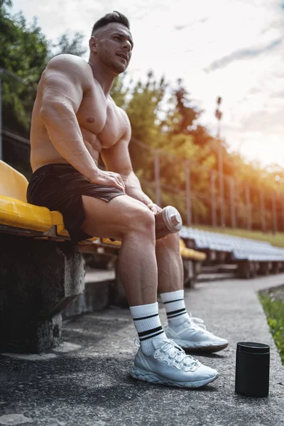 Suero de proteína en contenedor negro y hombre atlético sentado con agitador al aire libre —  Fotos de Stock