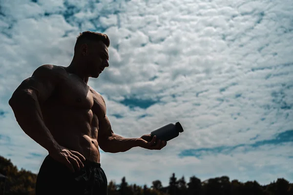 Muskulöser Athlet Mann hält Behälter mit Eiweißpulver oder Vitamin im Freien — Stockfoto