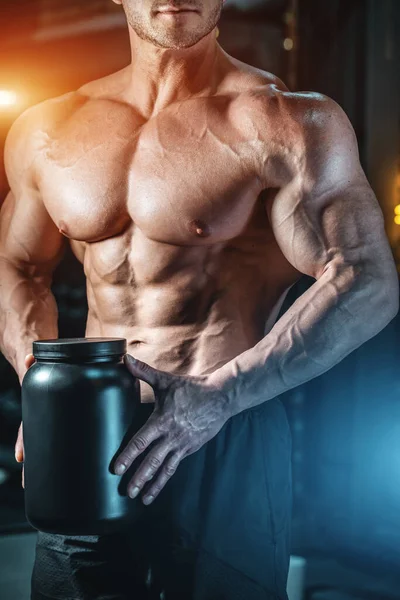 Крупный план мышечного спортсмена, держащего черный контейнер с белковой добавкой сыворотки — стоковое фото