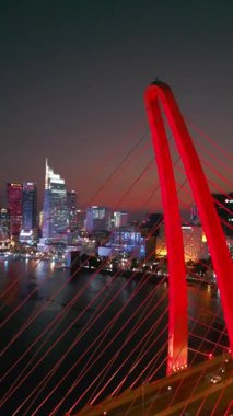 Saigon nehri üzerinde aydınlatma ışıkları olan modern köprü, arka planda finans merkezi, Ho Chi Minh şehri, Vietnam hava aracı manzaralı. Yüksek kalite 4k görüntü, dikey video