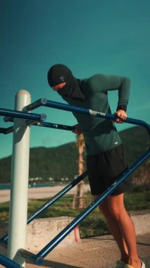 Erkek vücut geliştirici gün batımında paralel barlarda dalış yapıyor, Sporcu adam gün batımında açık hava ekipmanlarıyla trisepsleri eğitiyor. Yüksek kalite 4k görüntü