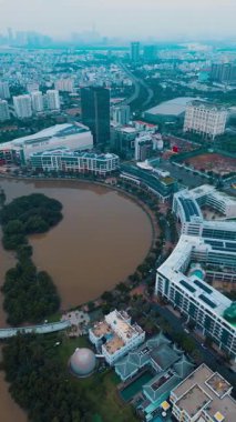 Ho Chi Minh şehrinin hilal gölü ve yeşil parkı, su birikintisi ve Asya Saigon şehrinin modern yerleşim bölgesi, hava aracı üst görünümü. Yüksek kalite 4k görüntü, dikey video