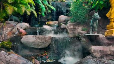Tropikal bahçede soğuk sis olan yapay şelale, taşların ve heykellerin arasında sis salan şelale. Yüksek kalite 4k görüntü