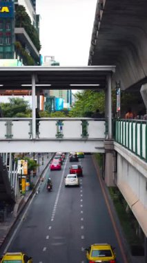 Bangkok sokak trafiği, yaya köprüsü altında günlük şehir hayatı, Bangkok 'ta şehir yolu, arabalar ve üst geçitteki insanlar, dikey video. Yüksek kaliteli görüntüler