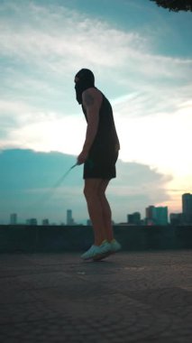 Günbatımı antrenmanı sırasında nehir kıyısında ip atlayan erkek vücut geliştirici güneş batımında atlama ipiyle atlama antrenmanı yapan atlet, 4k dikey video egzersizi için ejderha köprüsü üstüne atlama eğitimi. Yüksek kalite 4k görüntü