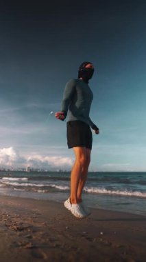 Gün batımında deniz kenarında ip atlayan vücut geliştirici atlama antrenmanı güneş batımında okyanus kıyısında ip atlama antrenmanı, dikey video 4k. Yüksek kalite 4k görüntü