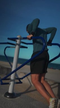 Erkek vücut geliştirici gün batımında paralel barlarda dalış yapıyor, Sporcu adam gün batımında açık hava ekipmanlarıyla trisepsleri eğitiyor. Yüksek kalite 4k görüntü