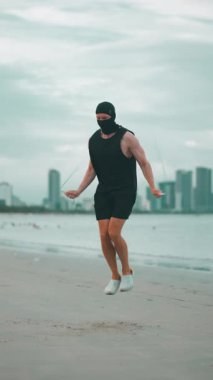 Şehir arka planında günbatımı egzersizi sırasında deniz kenarında ip atlayan erkek vücut geliştirici, kardiyo egzersizi için okyanus kıyısında atlama ipi kullanan atlet erkek antrenmanı, dikey video 4k. Yüksek kaliteli görüntüler