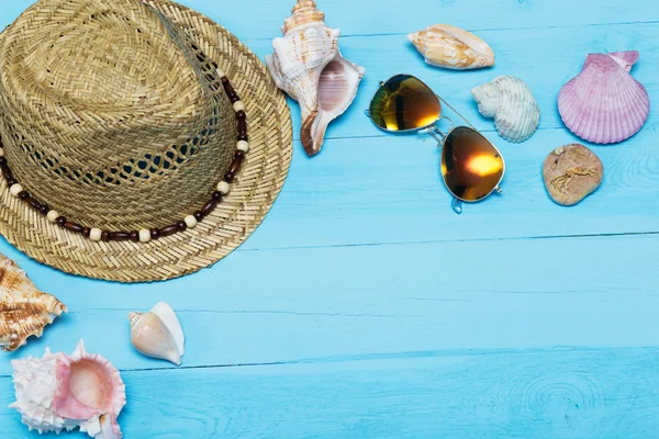 Muscheln, Hut und Sonnenbrille auf blauem Holzgrund — Stockfoto