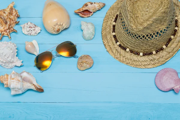 Muscheln, Hut und Sonnenbrille auf blauem Holzgrund — Stockfoto