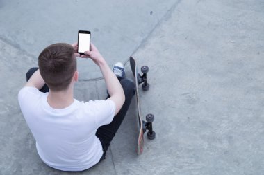 Akıllı telefon kullanarak paten kurulu oturan genç adam