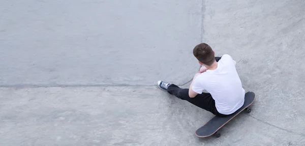 Mladý muž v tričku a džínách, sedí na skateboard — Stock fotografie