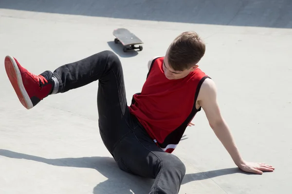 Młody człowiek odpada planszę skate, siedząc na konkretne ziemi. — Zdjęcie stockowe