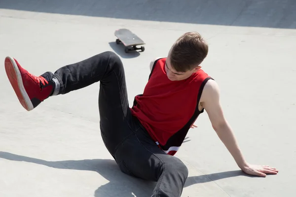 Junger Mann stürzt von Skateboard und sitzt auf Betonrampe. Stockfoto