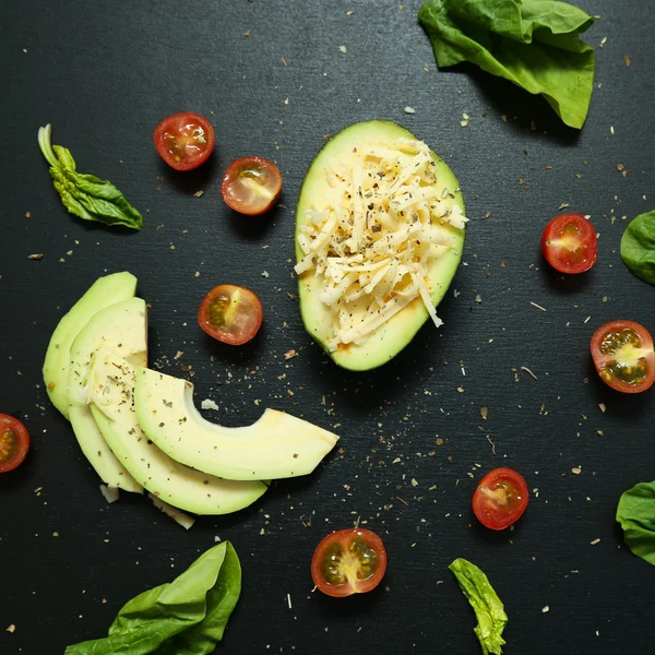 Sliced avocado and tomatoes, spinach leaves on black background.
